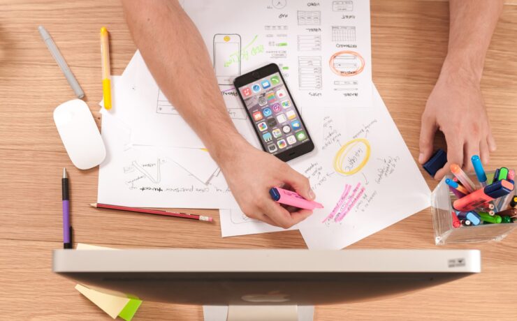 Persona resaltando las ideas adelante de un ordenador con móvil y bolígrafos sobre la mesa.